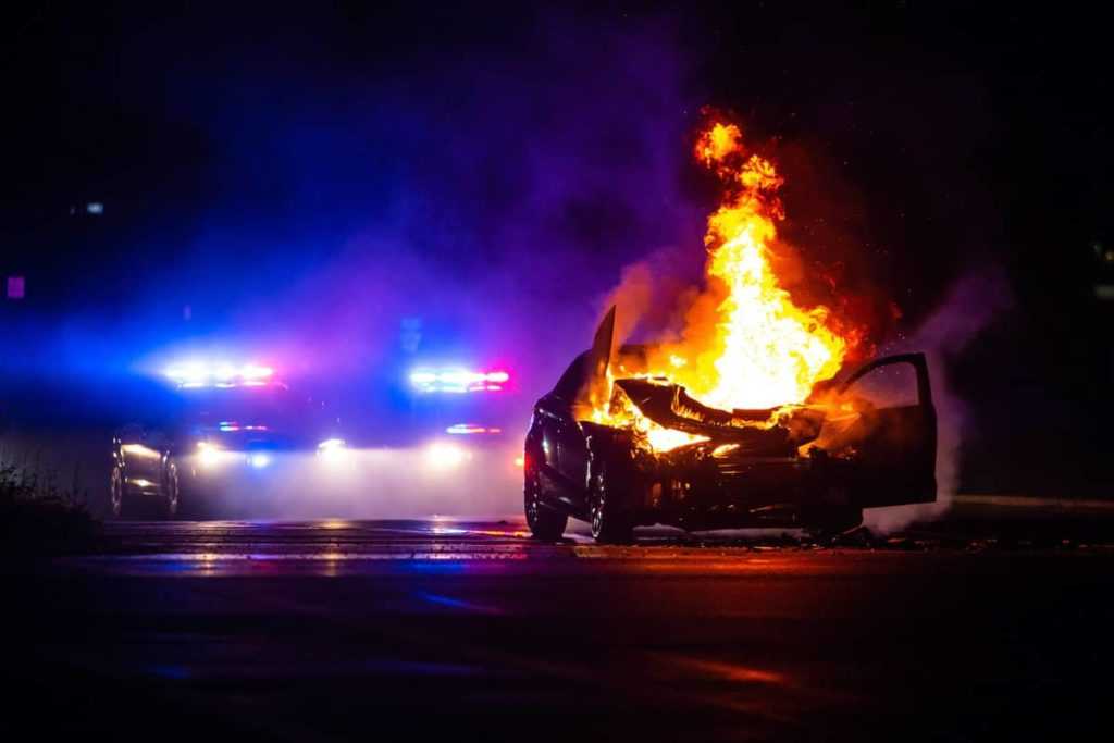 Car on fire at night with police lights in background