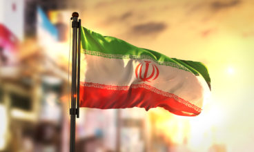 Iran Flag Against City Blurred Background At Sunrise Backlight