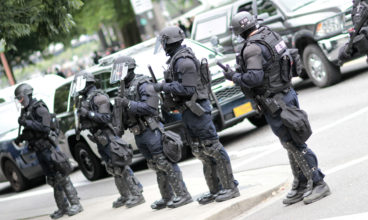 Police officers in riot gear overseeing a crowd of protestors.