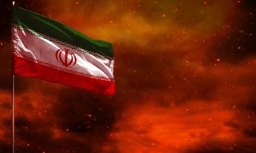 Fluttering Iran flag mockup with blank space for your text on crimson red sky with smoke pillars background. Troubles concept.