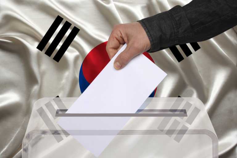male voter drops a ballot in a transparent ballot box against the background of the national flag of South Korea, concept of state elections, referendum