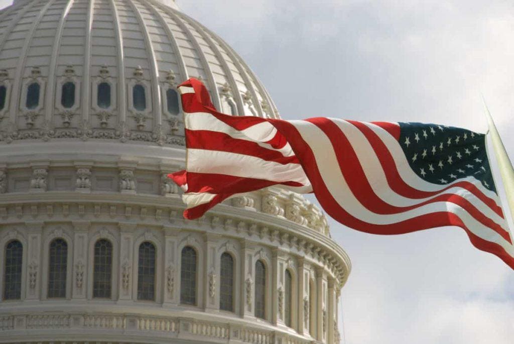 Beautiful flag of the United States of America waving with the strong wind and behind it the dome of the Capitol.