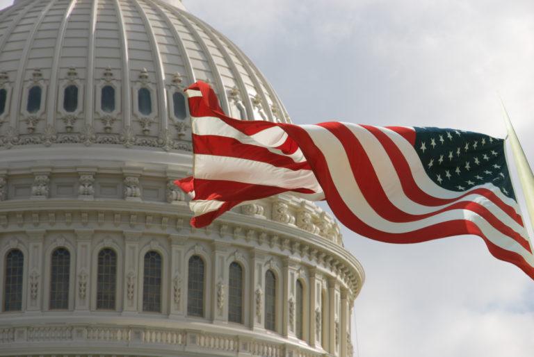 Beautiful flag of the United States of America waving with the strong wind and behind it the dome of the Capitol.