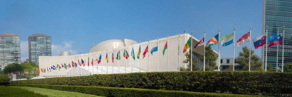 UN United Nations general assembly building with world flags fly - 3:1 aspect ratio