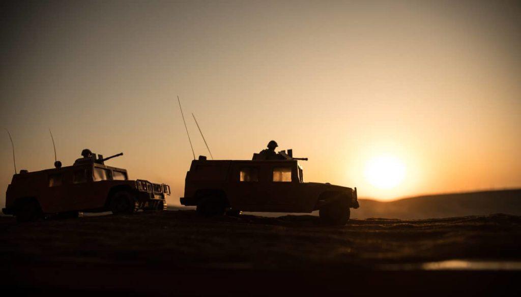 Military patrol car on sunset background. Army war concept. Silhouette of armored vehicle with soldiers ready to attack. Artwork decoration. Selective focus