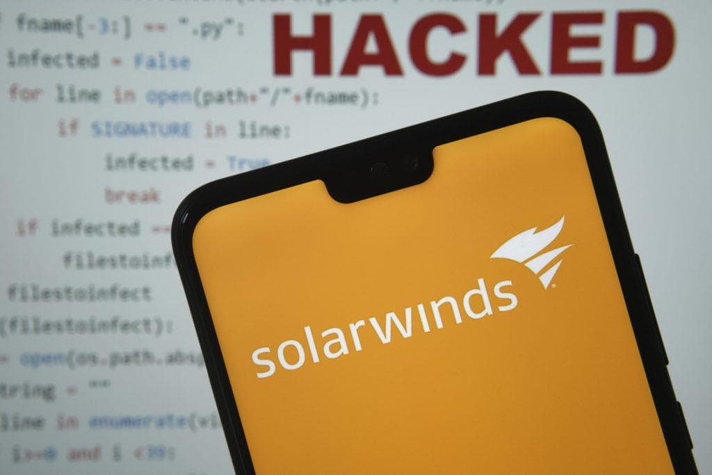 Solarwinds logo seen on the smartphone screen, with simple brute force attack code with HACKED word on the blurred background. NOT A MOTAGE, REAL PHOTO. Stafford, United Kingdom - December 24 2020.